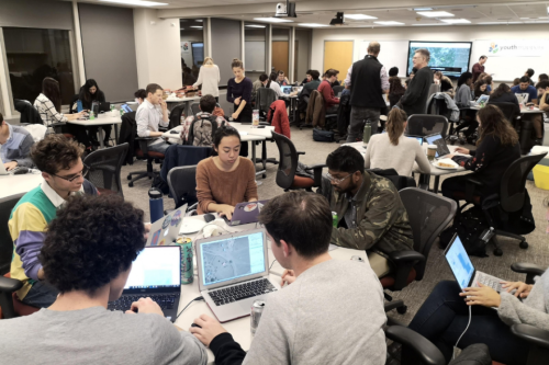 Students engaged in the Mapathon, sitting in a crowded room with maps on their laptop screens